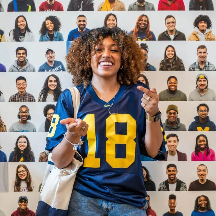 Zoe Wright is wearing a blue football sweatshirt with yellow numbers. She has brown skin, brown curly hair and she is smiling broadly.