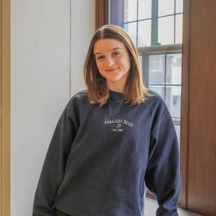 Quinn, the president of Amazin Blue, has blond hair and is wearing a blue sweatshirt that says Amazin' Blue.