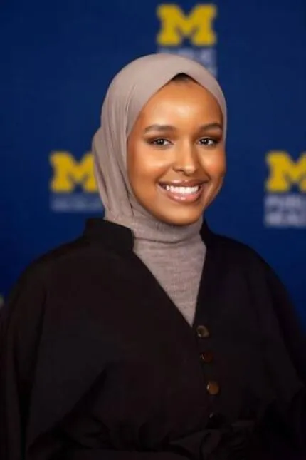 Farhia Mohamed is smiling broadly. She has brown skin and is wearing a tan hijab and a black sweater.